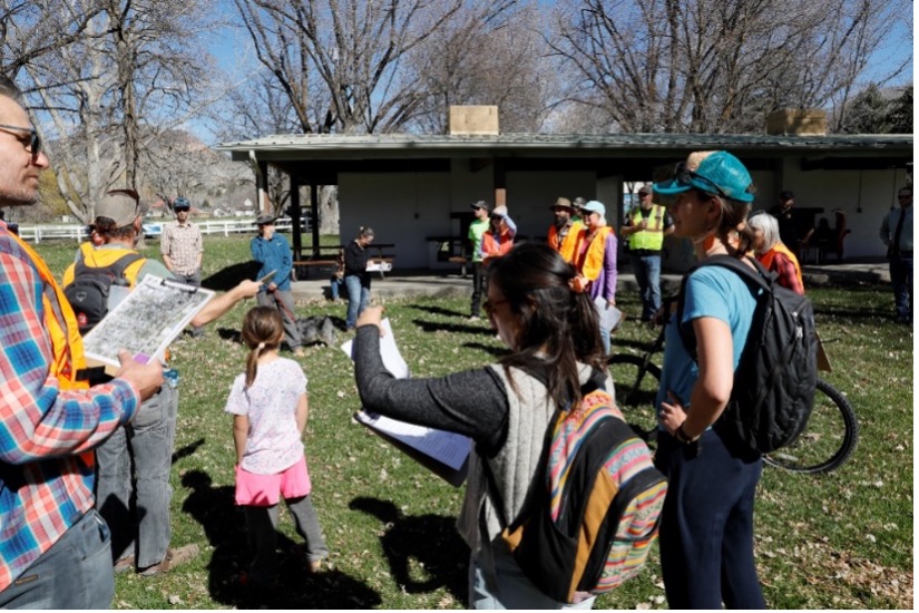 Children and adults standing in a field with a small shack behind them as they talk