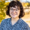 Girl with short hair and glasses standing outside smiling