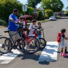 male with bike walking students with bikes across crosswalk